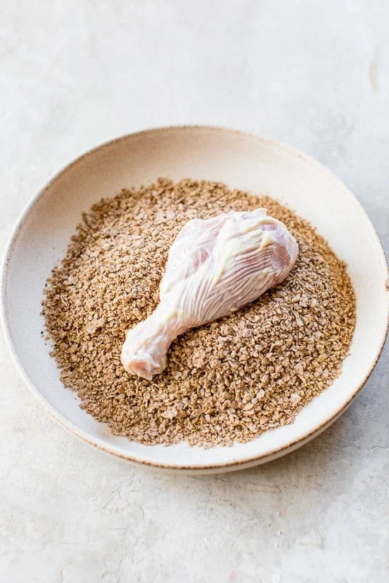 Chicken drumstick in bowl of bran flake coating.