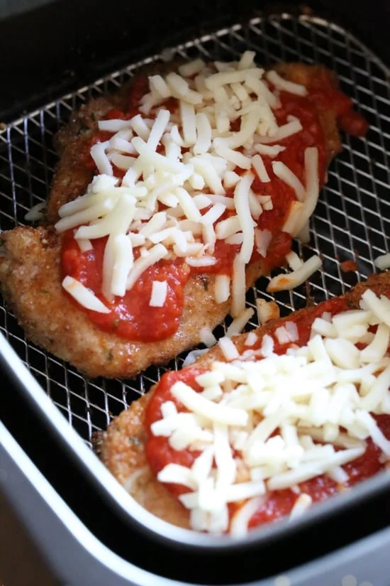 Chicken parmesan inside the air fryer topped with shredded mozzarella cheese.