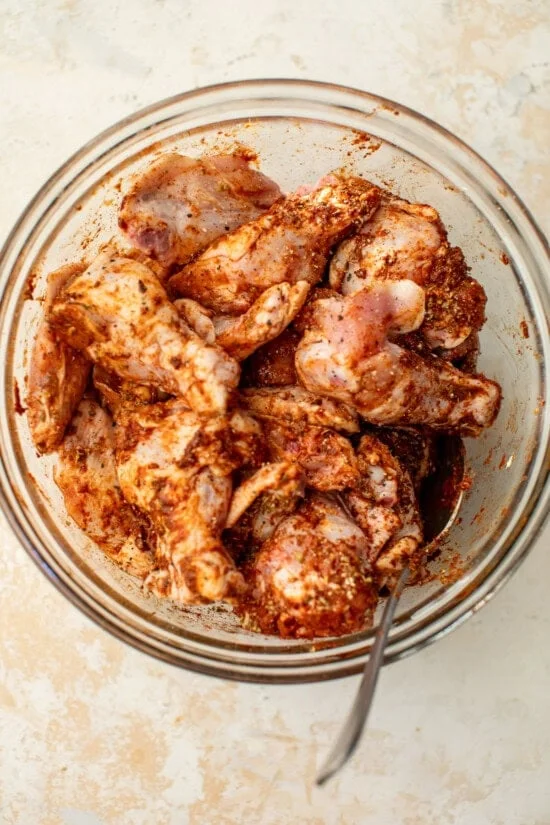 Chicken wings tossed in buffalo marinade in a bowl.