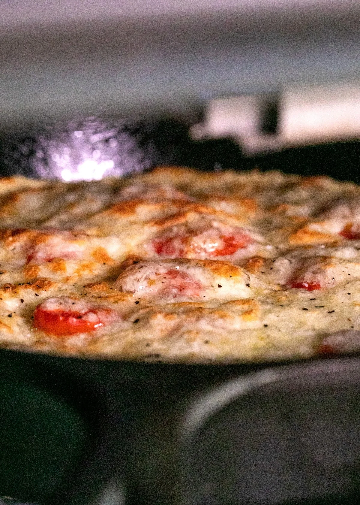 Chickpea pizza in cast iron skillet under oven's broiler