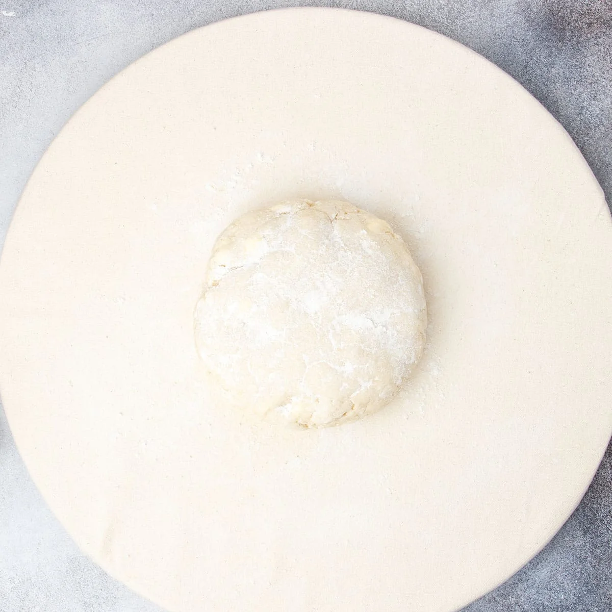 Chilled scone dough dusted with flour on tan cloth covered round ready to roll out.