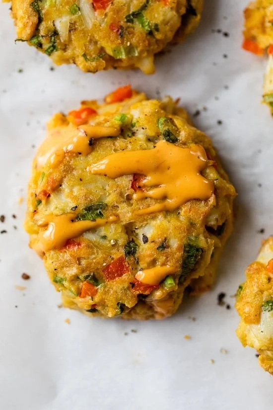 Close up of a baked lump crab cake drizzled with red pepper sauce.