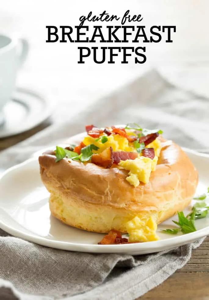 Close up of a breakfast puff on a white plate that has eggs, herbs and bacon bits on top