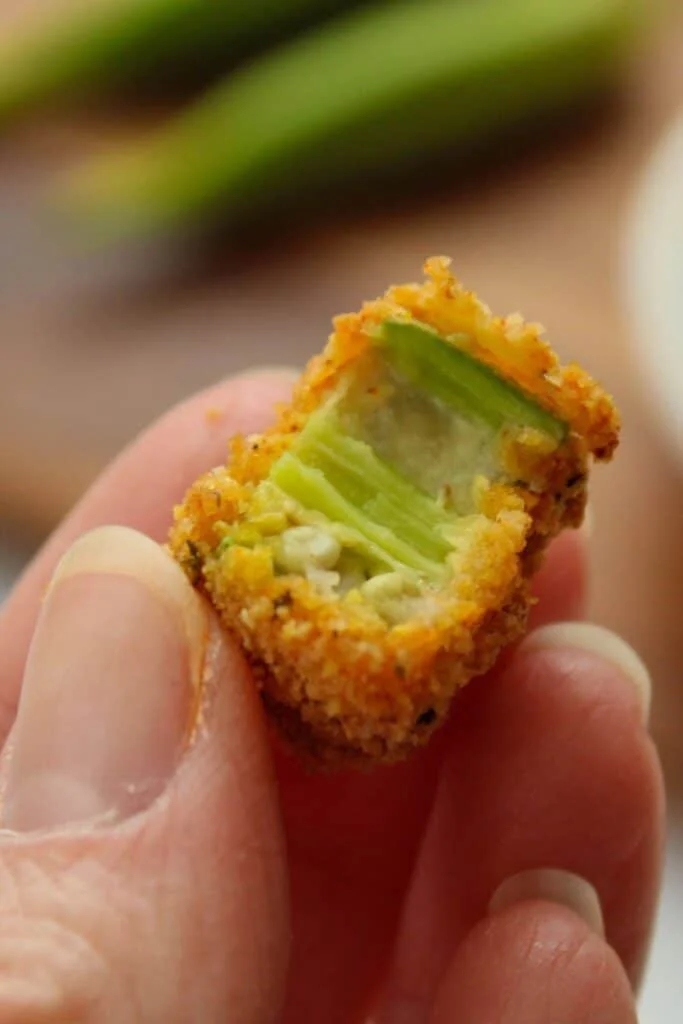 Close up of a hand holding air fryer okra with a bite taken out of it.