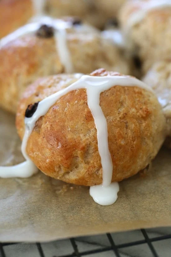 Close up of a hot cross bun topped with icing on a parchment-lined rack.