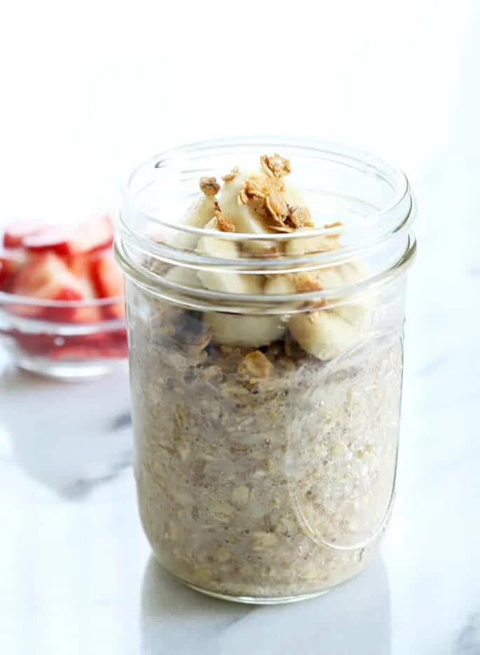 Close up of a jar with overnight oats, bananas and peanut butter on marble surface 