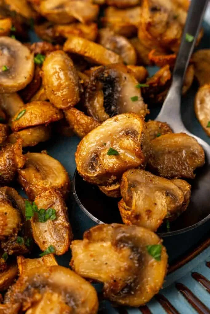 Close up of air fried mushrooms on a serving plate with a serving spoon.
