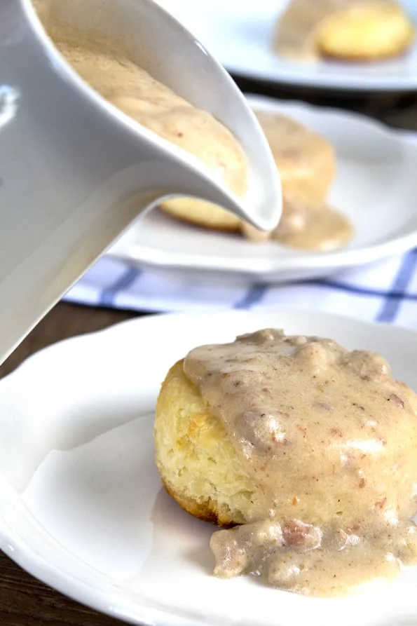 Close up of gravy being poured on biscuit.