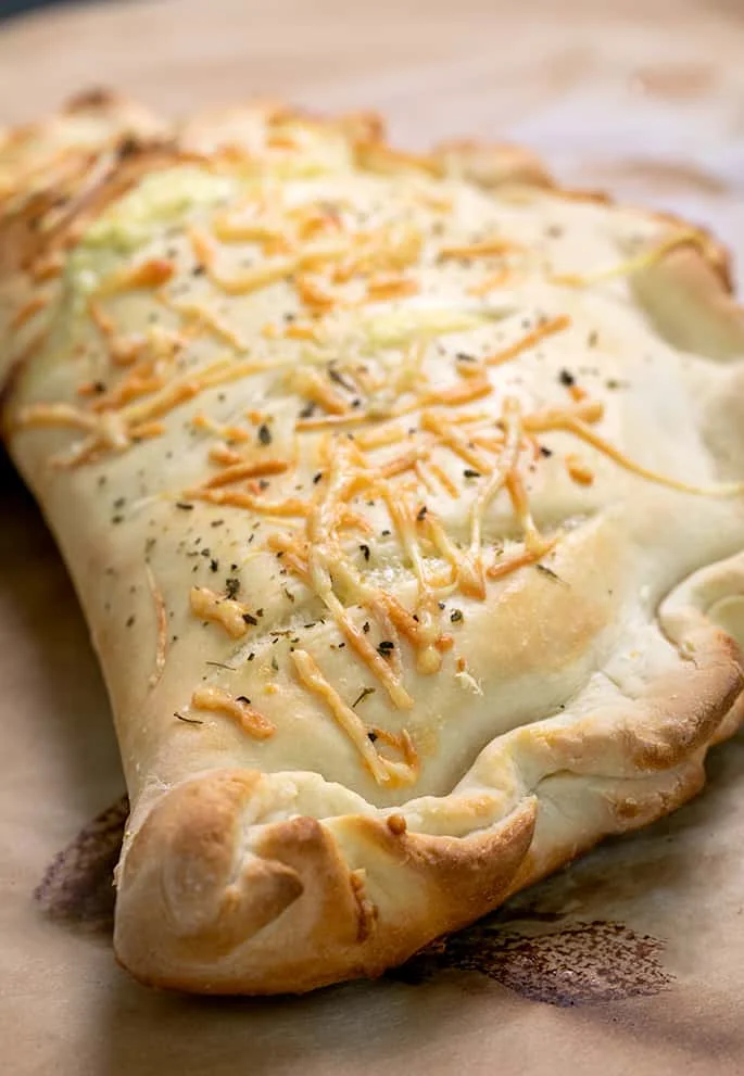 Close up of whole baked calzone uncut on brown paper