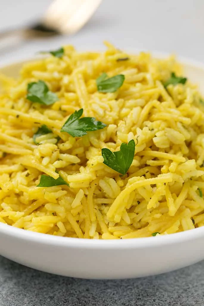 Closeup image from the side of rice a roni with fresh parsley in white round bowl with fork in background