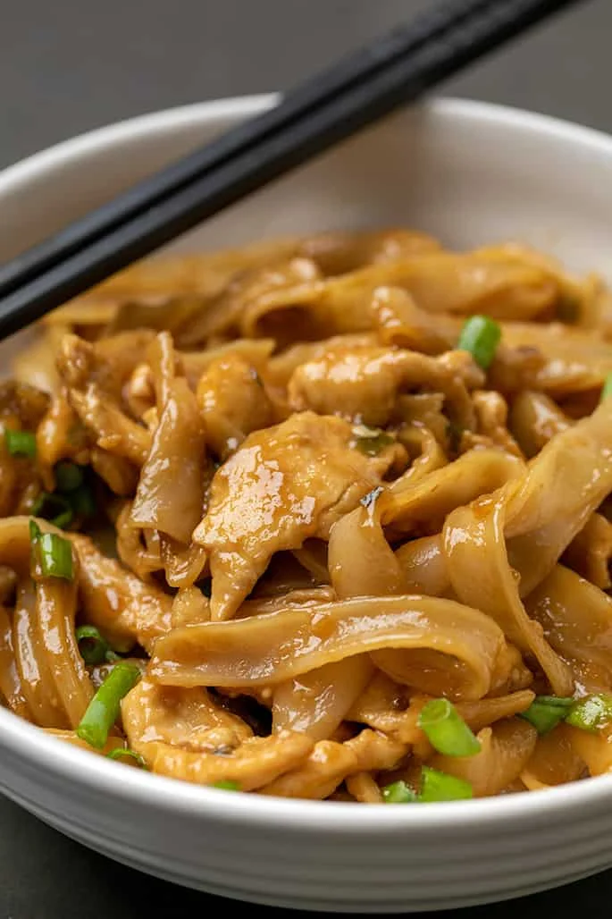 Closeup image of chicken in pile of lomein in white bowl