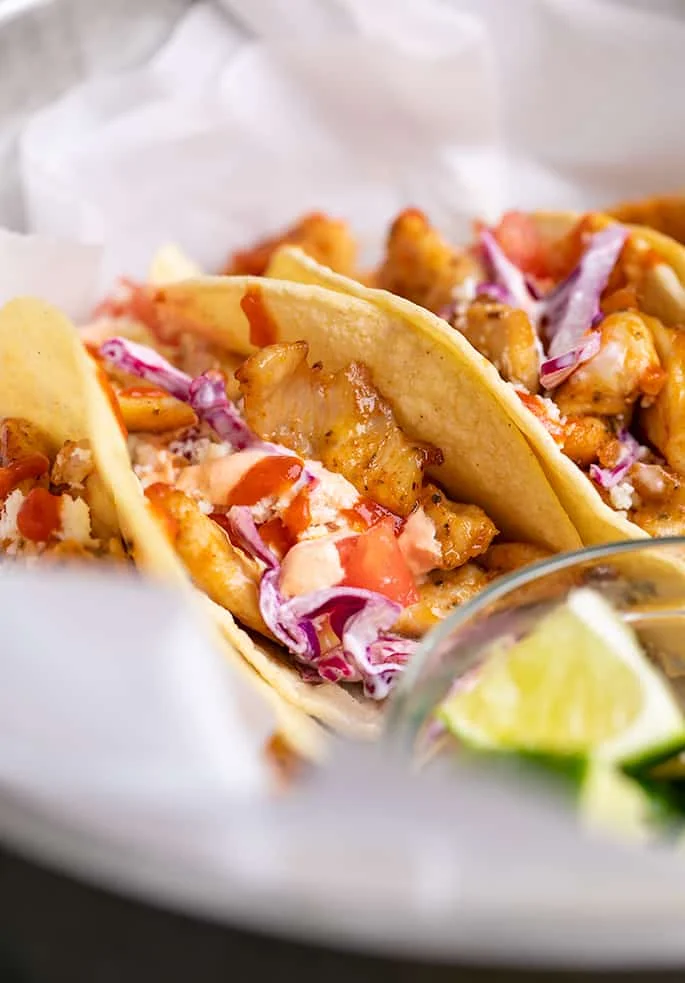Closeup image of cooked taco chicken, cheese, red sauce, and red cabbage in corn tortilla in white paper