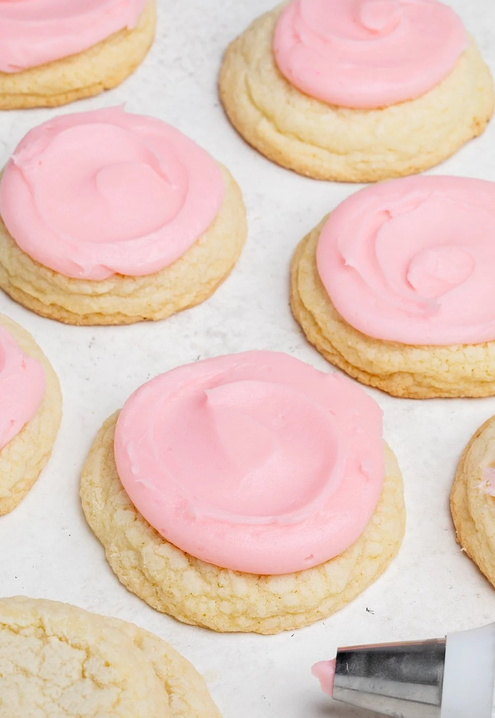 Closeup image of pink swirled frosting on top of round yellow cookie with pastry bag with pink frosting