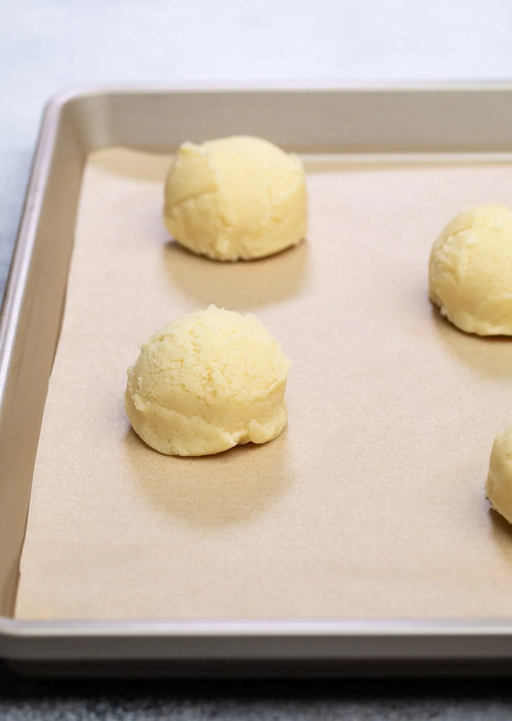 closeup image of round mounds of light yellow cookie dough on a baking sheet