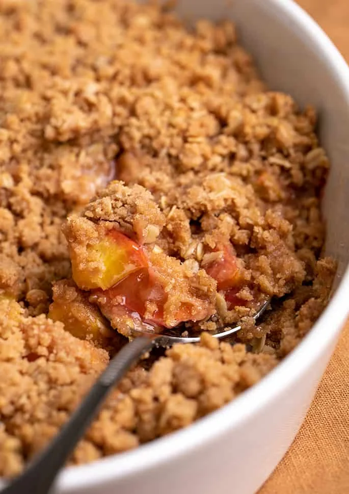 Closeup image of serving spoon in white serving dish of gluten free peach crisp