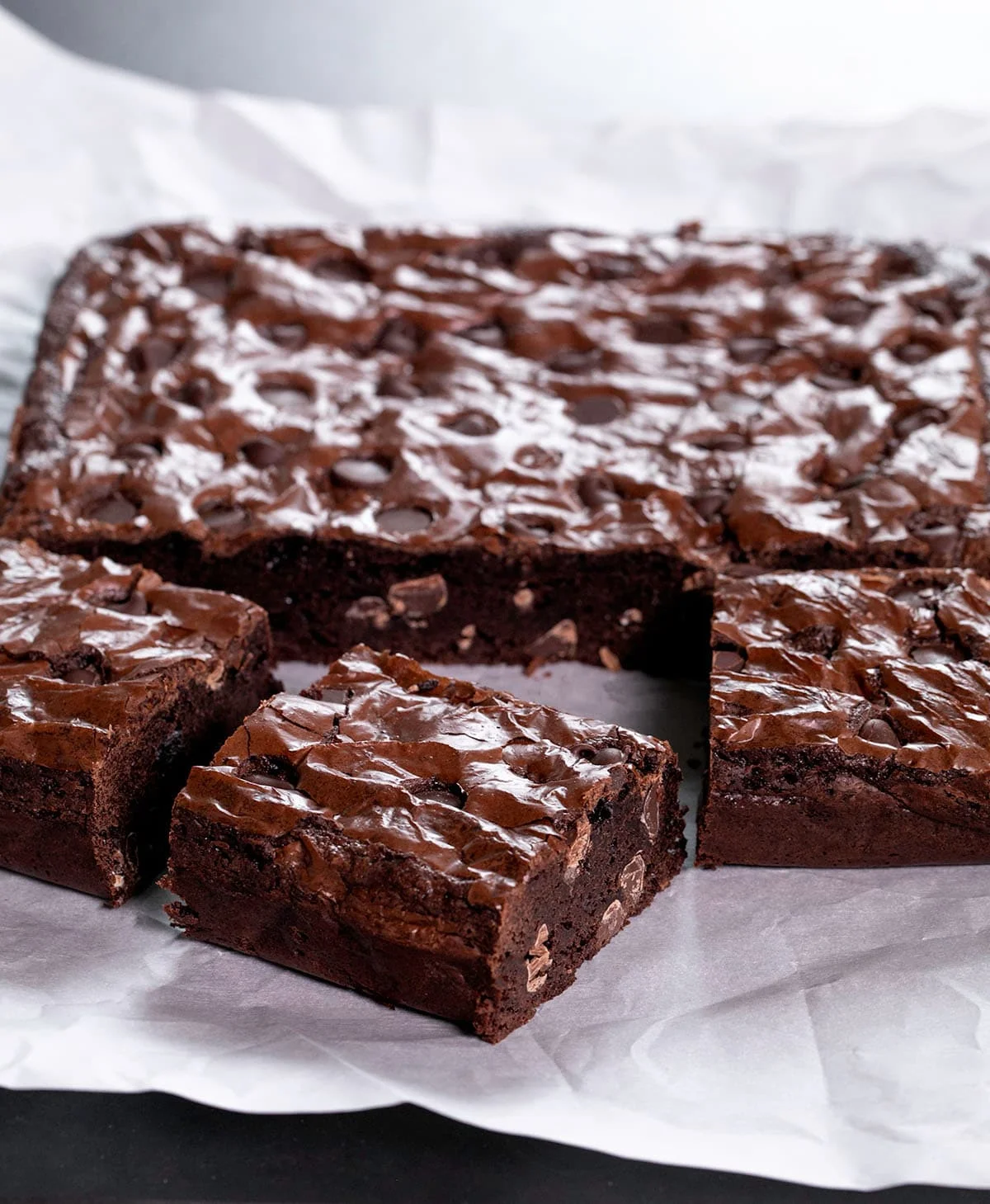 Closeup image of sliced brown squares with chocolate chips on white paper.