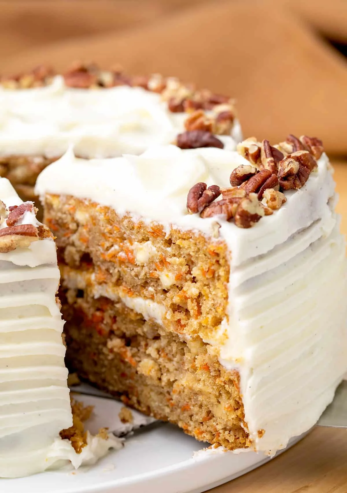 Closeup of a slice of the carrot cake being taken from whole cake on platter.