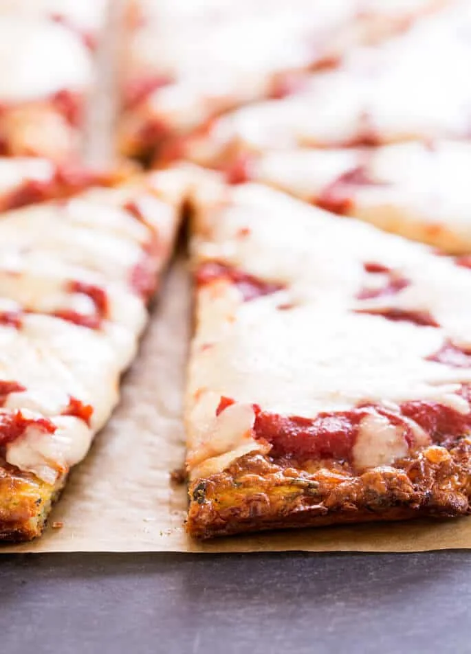 Closeup of crust of zucchini pizza crust slices with tomato sauce and cheese on brown paper