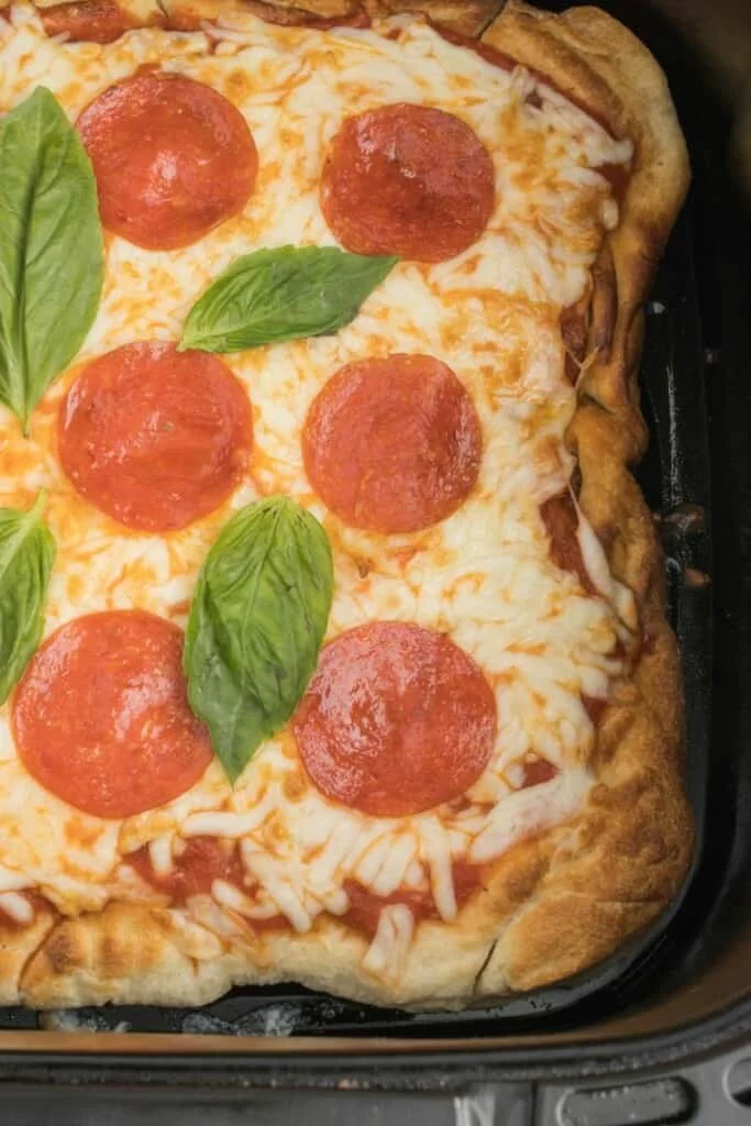 Closeup view of pepperoni pizza in a black air fryer basket.