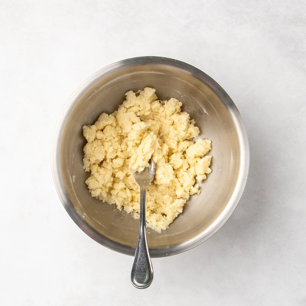 Clumpy pale dough mixture in a metal bowl with a fork.