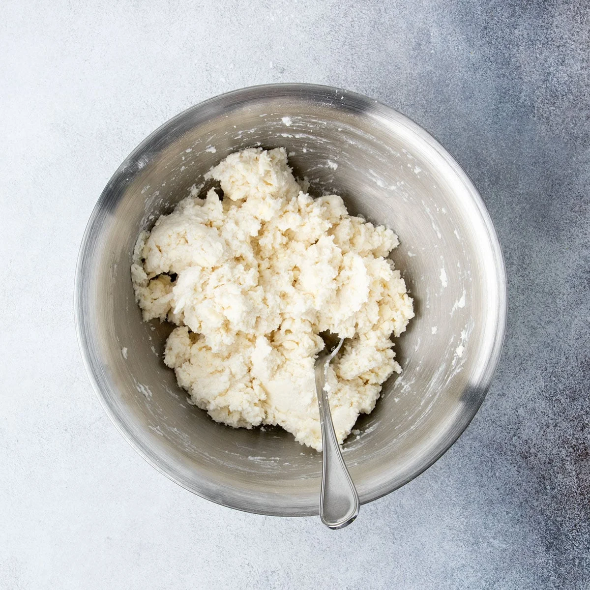 Coarse cobbler topping dough fully mixed and ready to be scooped, shown in a metal bowl.