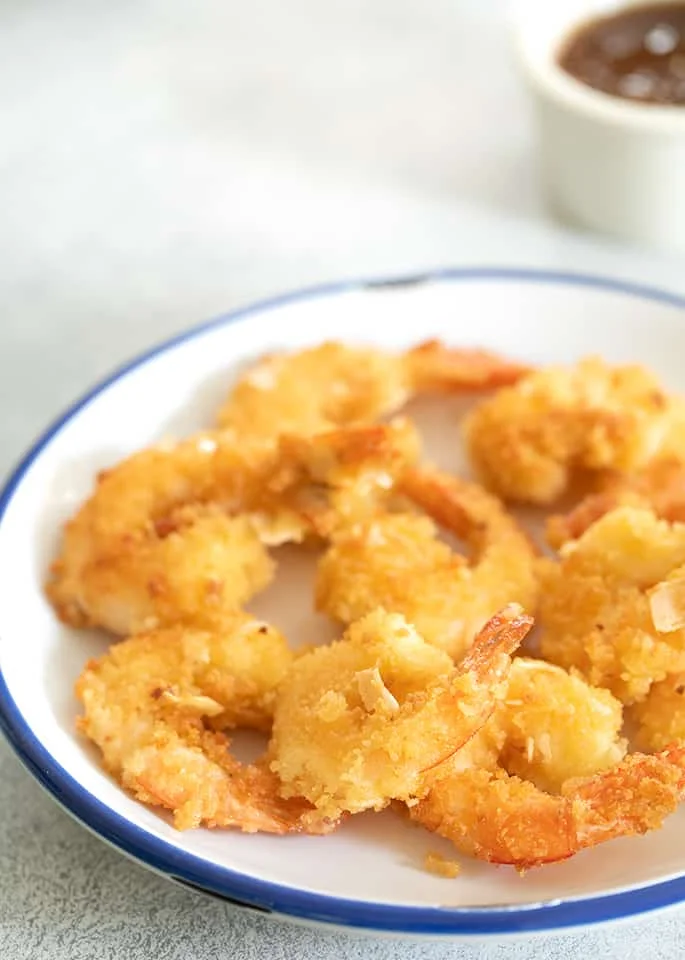 Coconut shrimp on white plate with sauce ramekin in the background