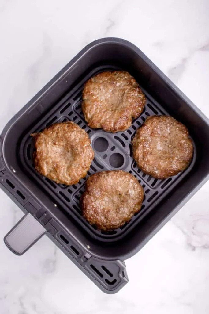 Cooked burgers in an air fryer basket.