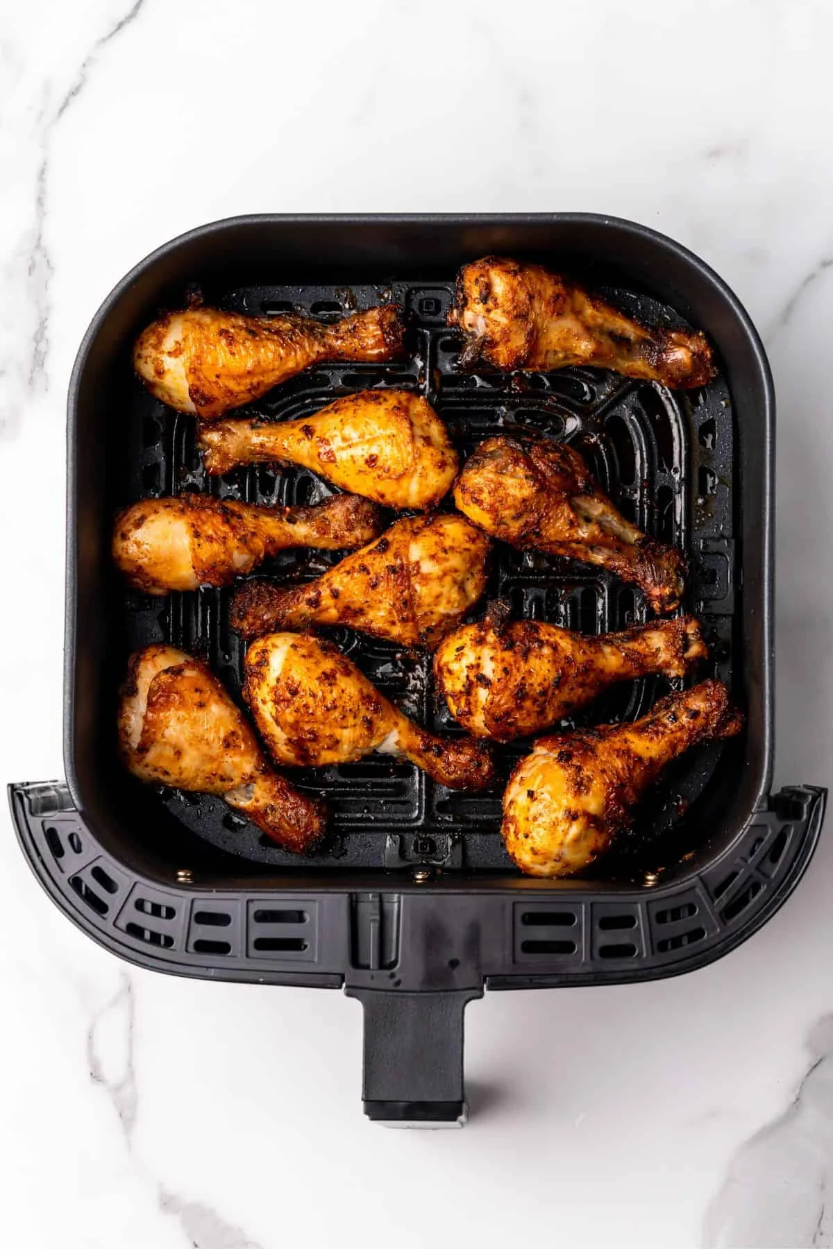 Cooked chicken legs in a square air fryer basket.