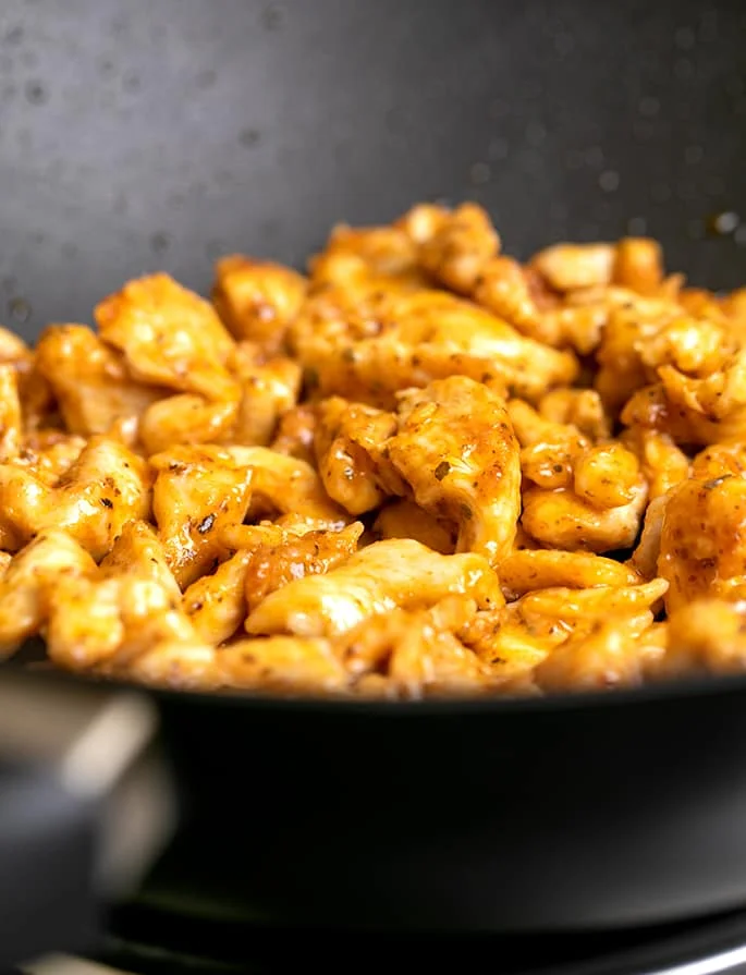 Cooked chicken pieces with red taco seasoning in black wok