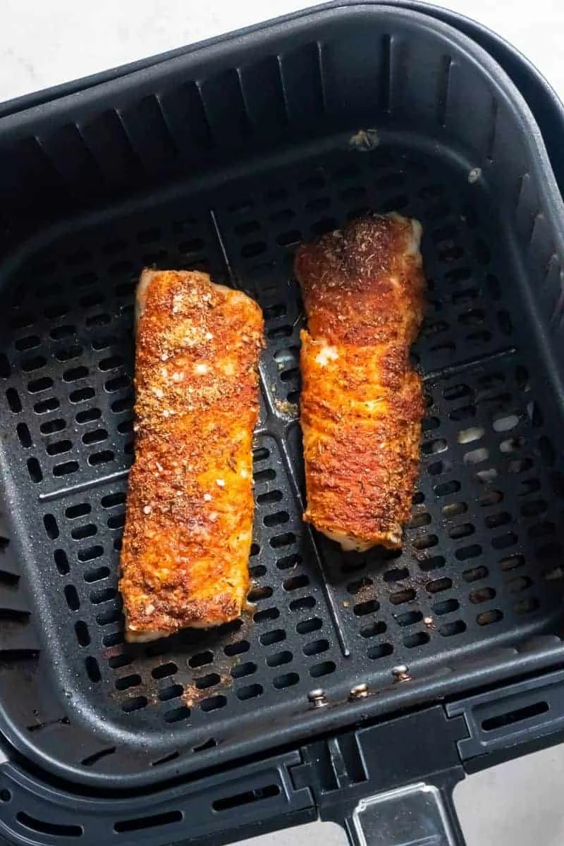 Cooked cod in a black air fryer basket.