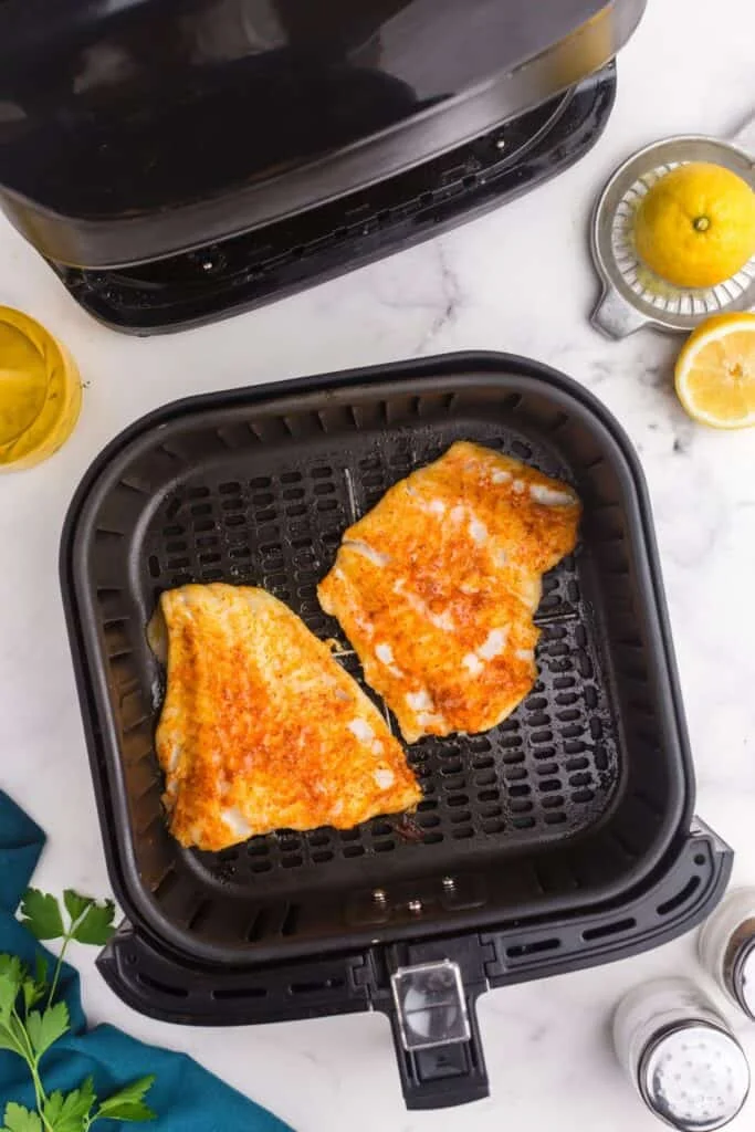 Cooked cod in an air fryer basket.