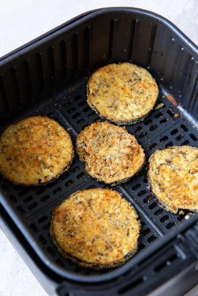 Cooked eggplant parmesan in an air fryer basket.
