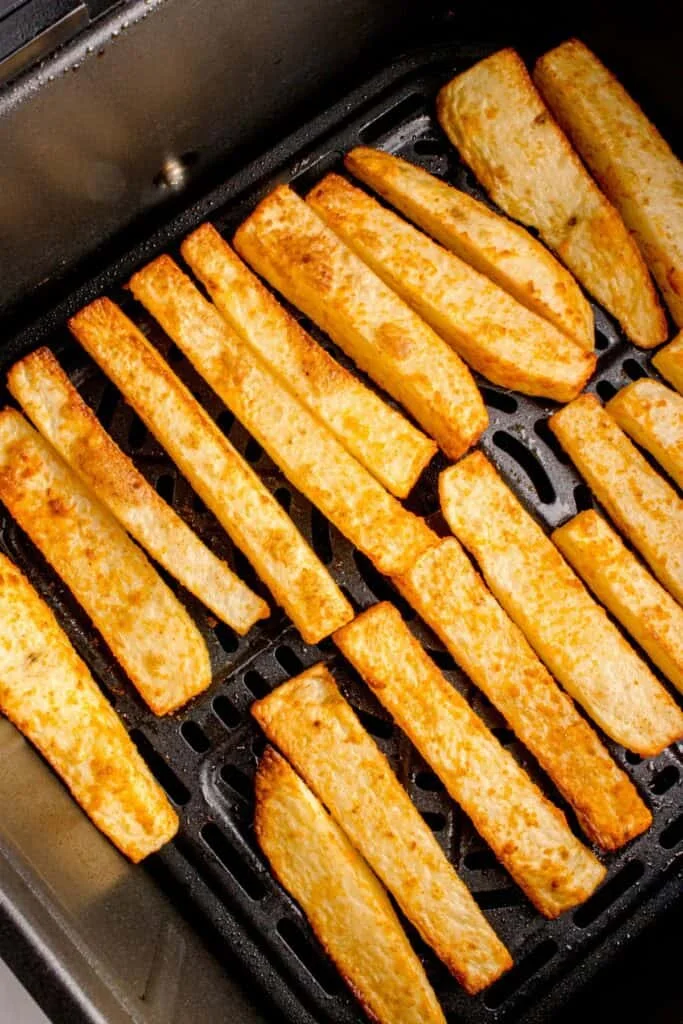 Cooked french fries in the air fryer basket with golden brown on the outside.