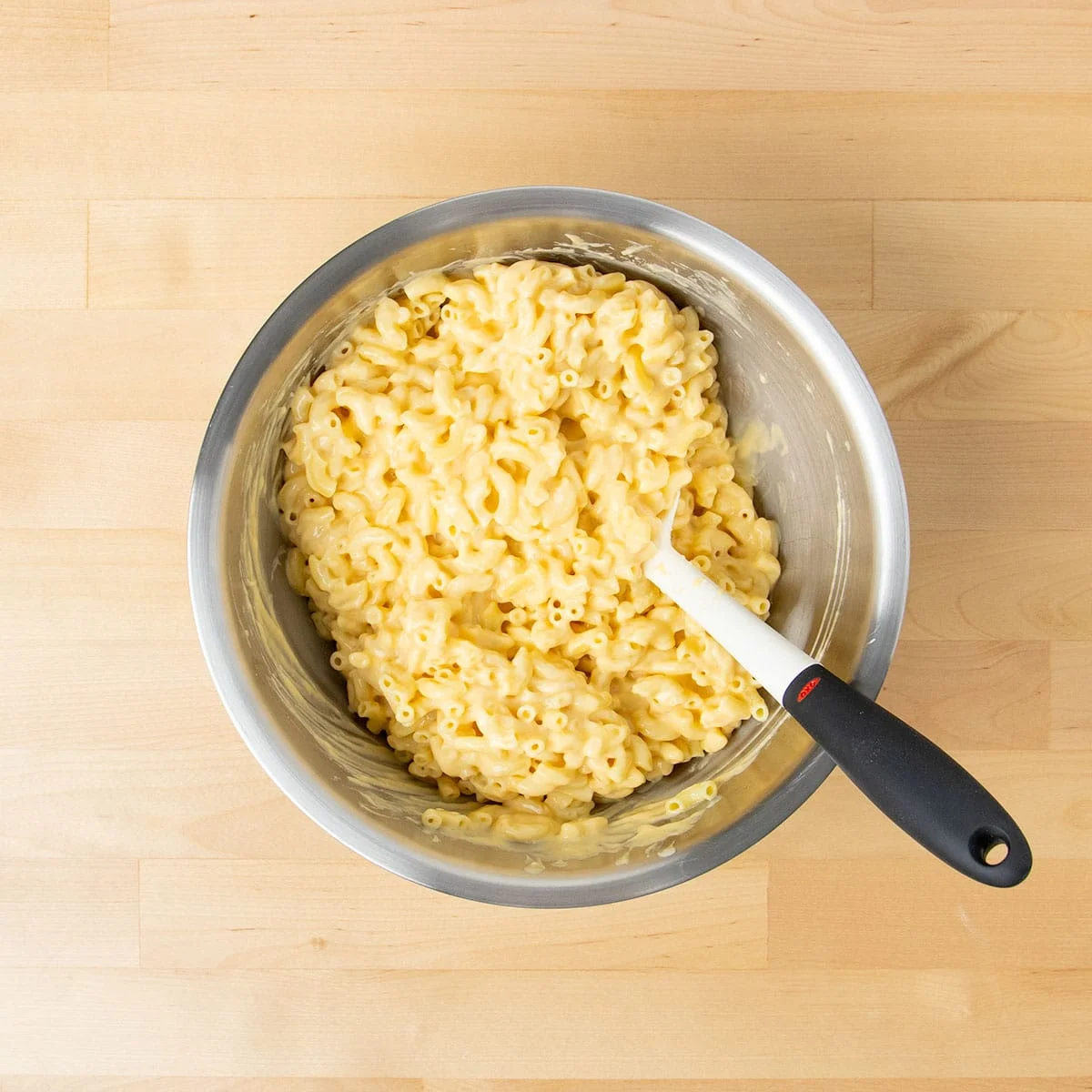 Cooked macaroni mixed with cheese sauce in mixing bowl with  spatula.