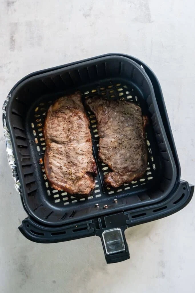 Cooked NY strip in an air fryer basket.