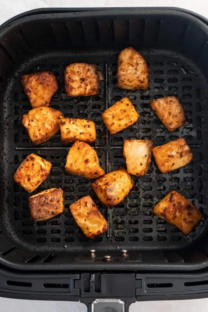 Cooked salmon bites in an air fryer basket.