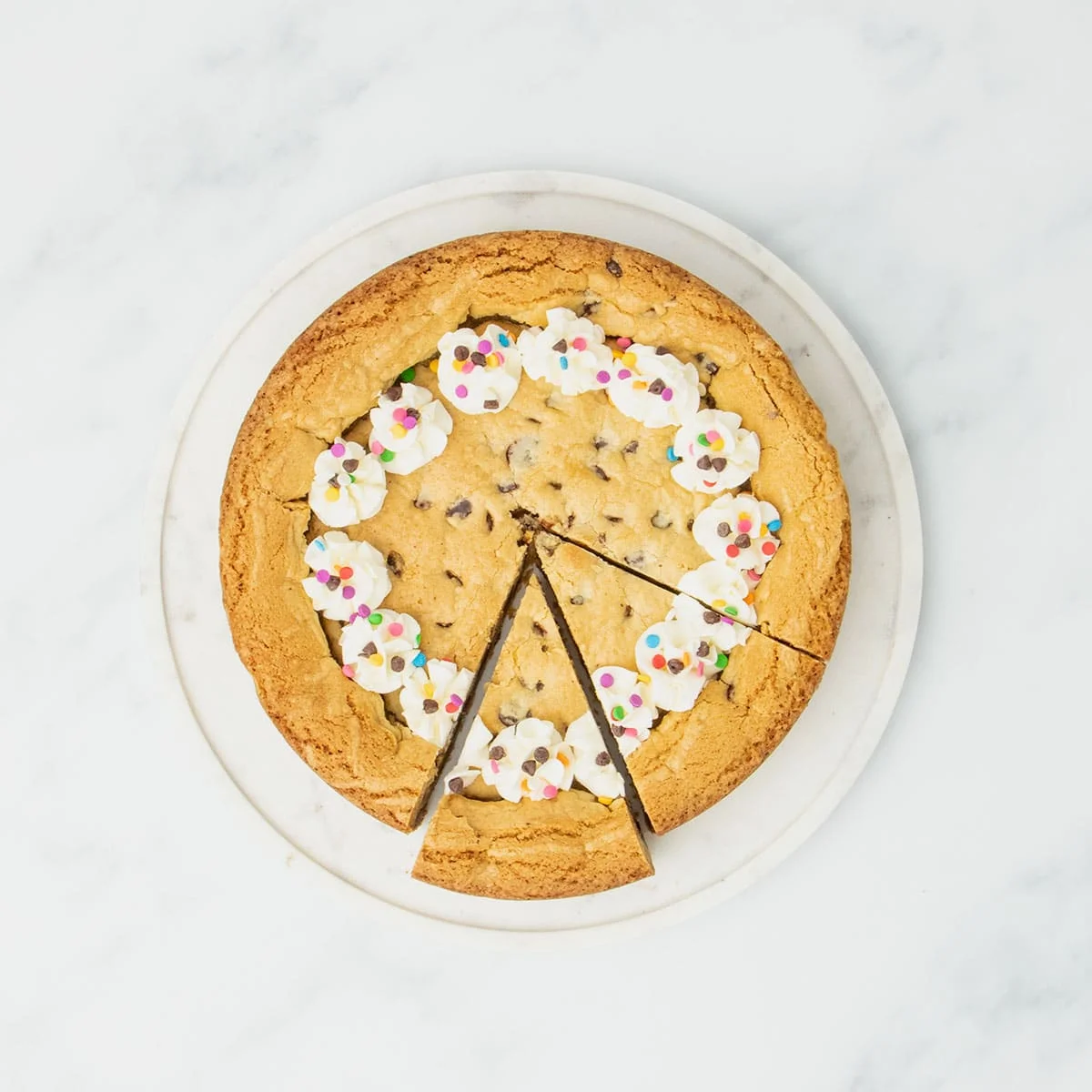 Cooled and decorated cookie cake with piped frosting rosettes and sprinkles, one slice partially pulled out