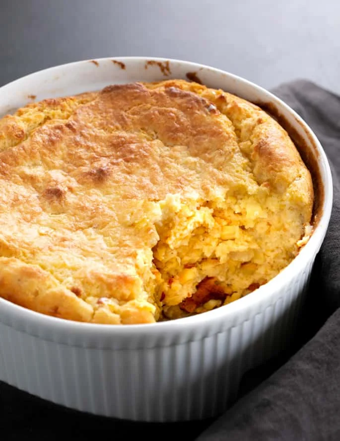 Cornmeal spoonbread in a casserole dish baked with a serving removed.