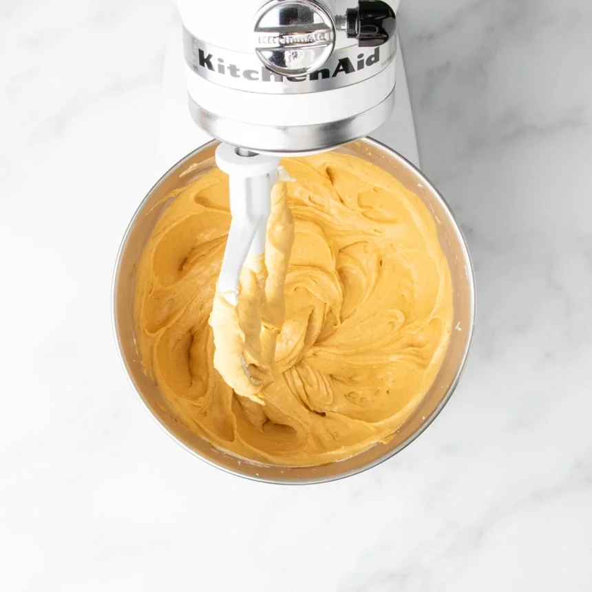 Cream cheese filling with added pumpkin puree, pumpkin spice, and vanilla making it orange colored, being mixed until smooth in a stand mixer bowl.