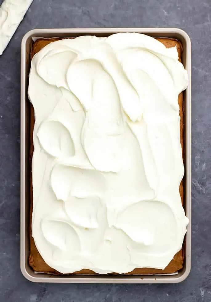 Cream cheese frosting spread in swoopy pattern on top of pumpkin bars in jelly roll pan