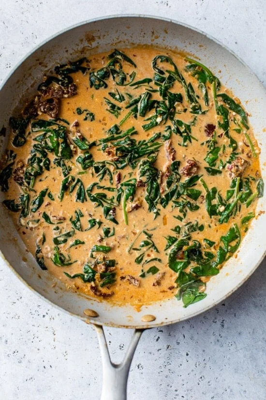 Creamy Marry Me Chicken sauce with sun-dried tomatoes and spinach in a skillet.