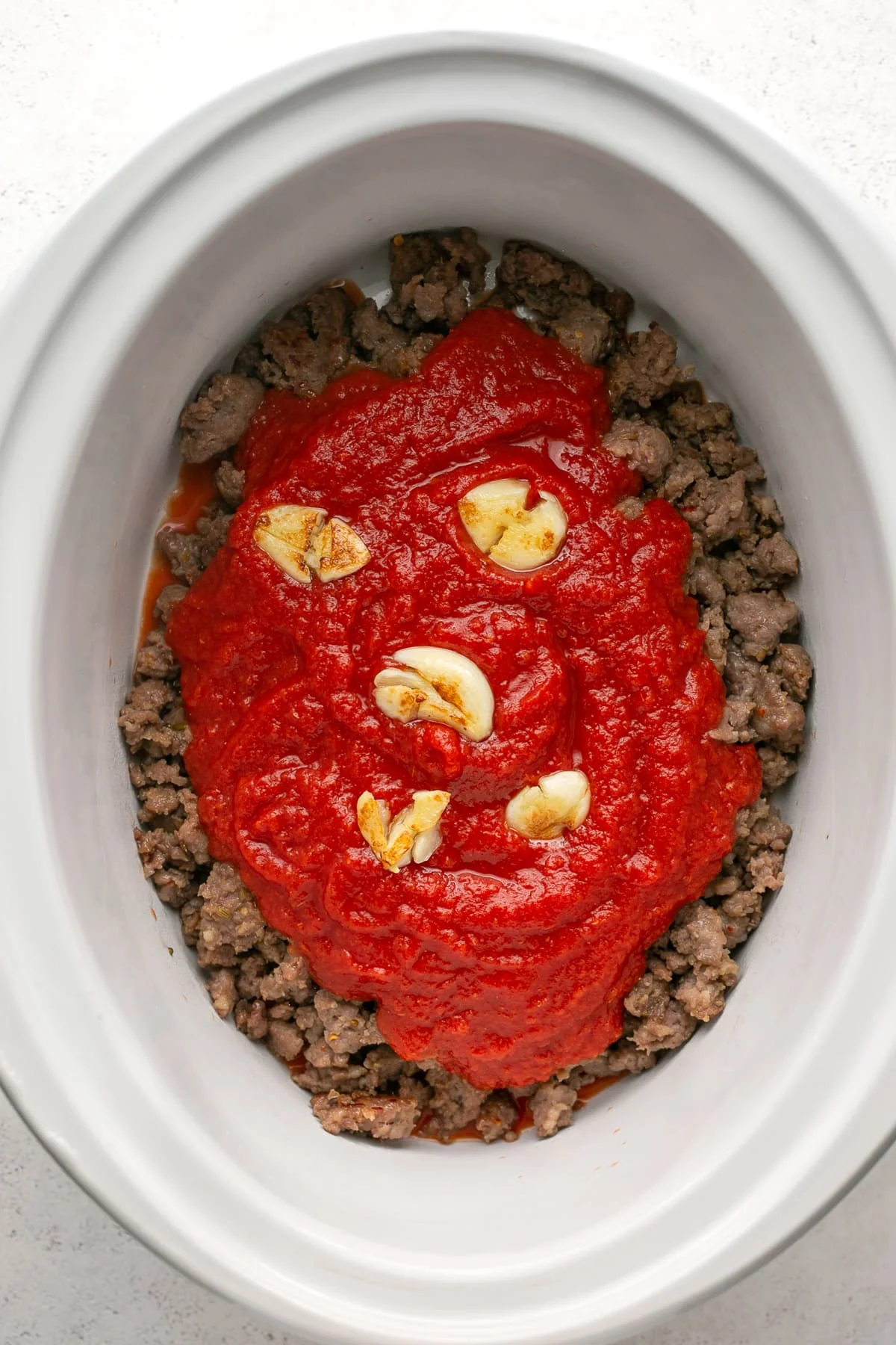 Crushed tomatoes and garlic added to ground sausage in the crock pot.