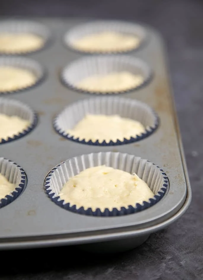 Cupcake batter in blue liners in muffin tin.