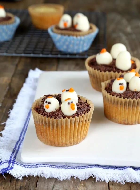 Cupcakes in brown wrappers with 3 molded chocolate chick heads on each, all on white surface