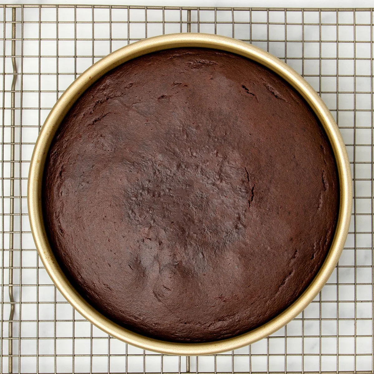 dark brown baked cake in same gold round pan on wire rack