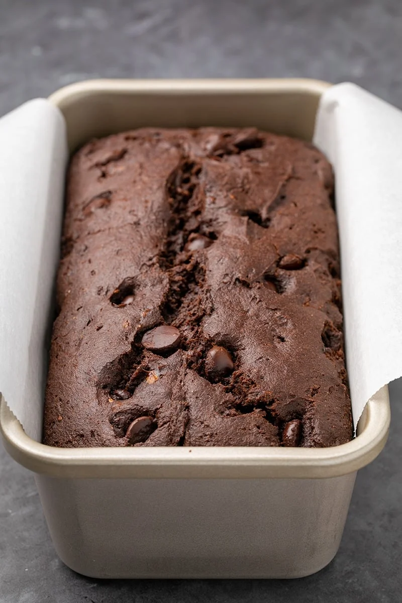 Dark brown cake in a white paper lined metal loaf pan.