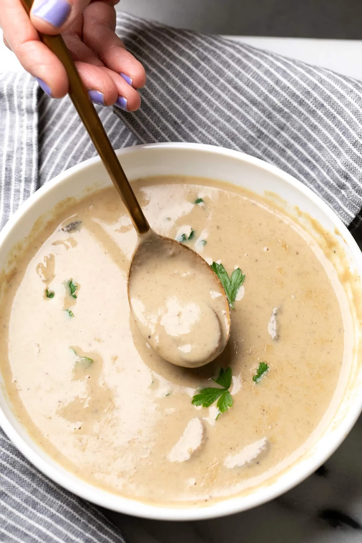 ding a soup spoon with cream of mushroom soup from a round white bowl of soup