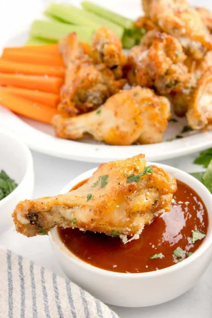dipping crispy air fryer chicken wings into a bbq sauce 