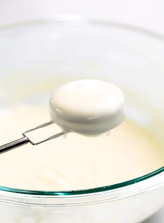 Dipping fork holding Oreo dipped in raw pancake batter held over glass bowl of batter