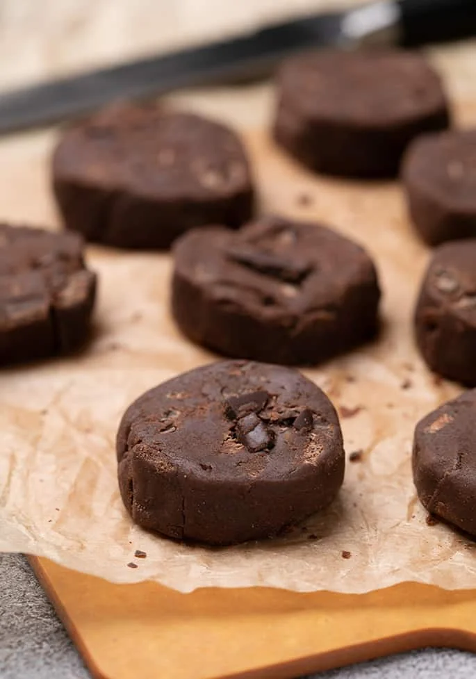 Disks of brown cookie dough on light brown paper on cutting board